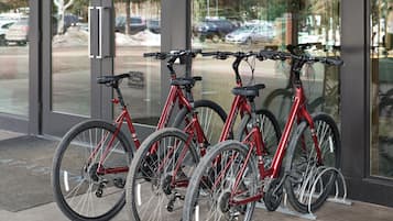 A row of red bicycles parked indoors, with a glass door leading to a parking area outside.
