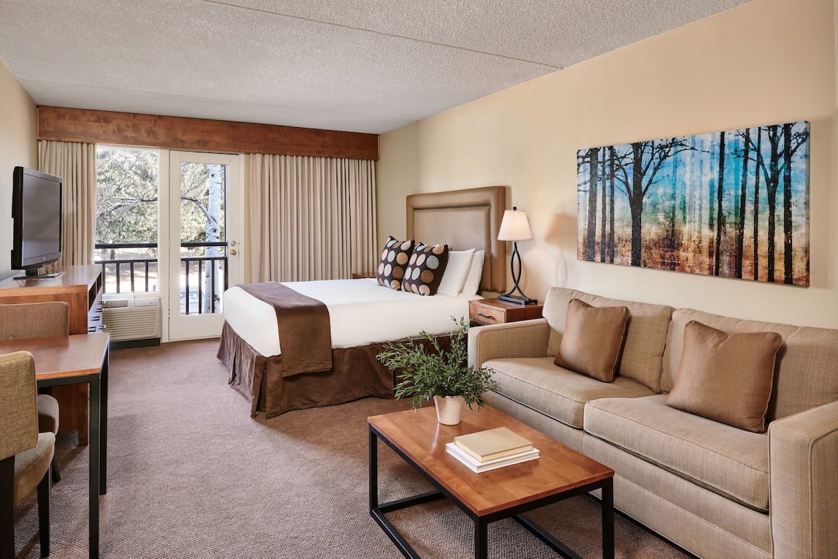 A hotel room with a bed, a sofa, a coffee table, a TV, and a painting on the wall.
