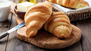Des croissants sur une planche en bois, accompagnés d’un couteau, d’un bol de beurre et d’un pot de miel.