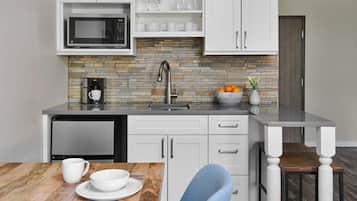 Una cocina moderna con armarios blancos, microondas integrado, cafetera y un lavamanos.