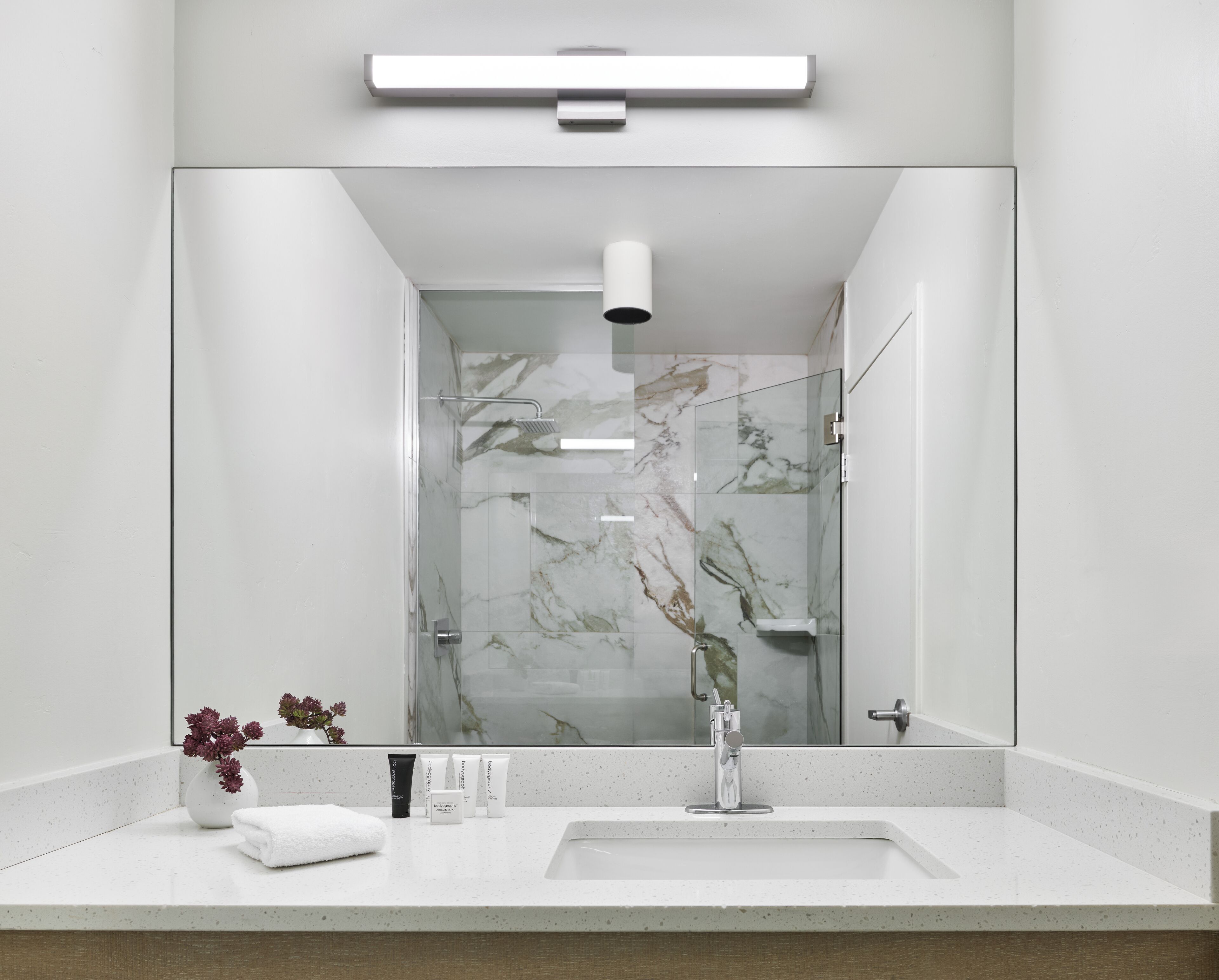 Un bagno moderno con uno specchio grande, una doccia e un lavandino.