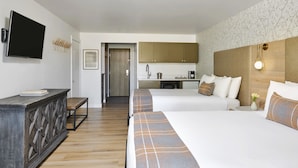 A hotel room with a large bed, a bedside table, a TV mounted on the wall, and a view into the kitchen area. - The Inn at Aspen (Aspen)