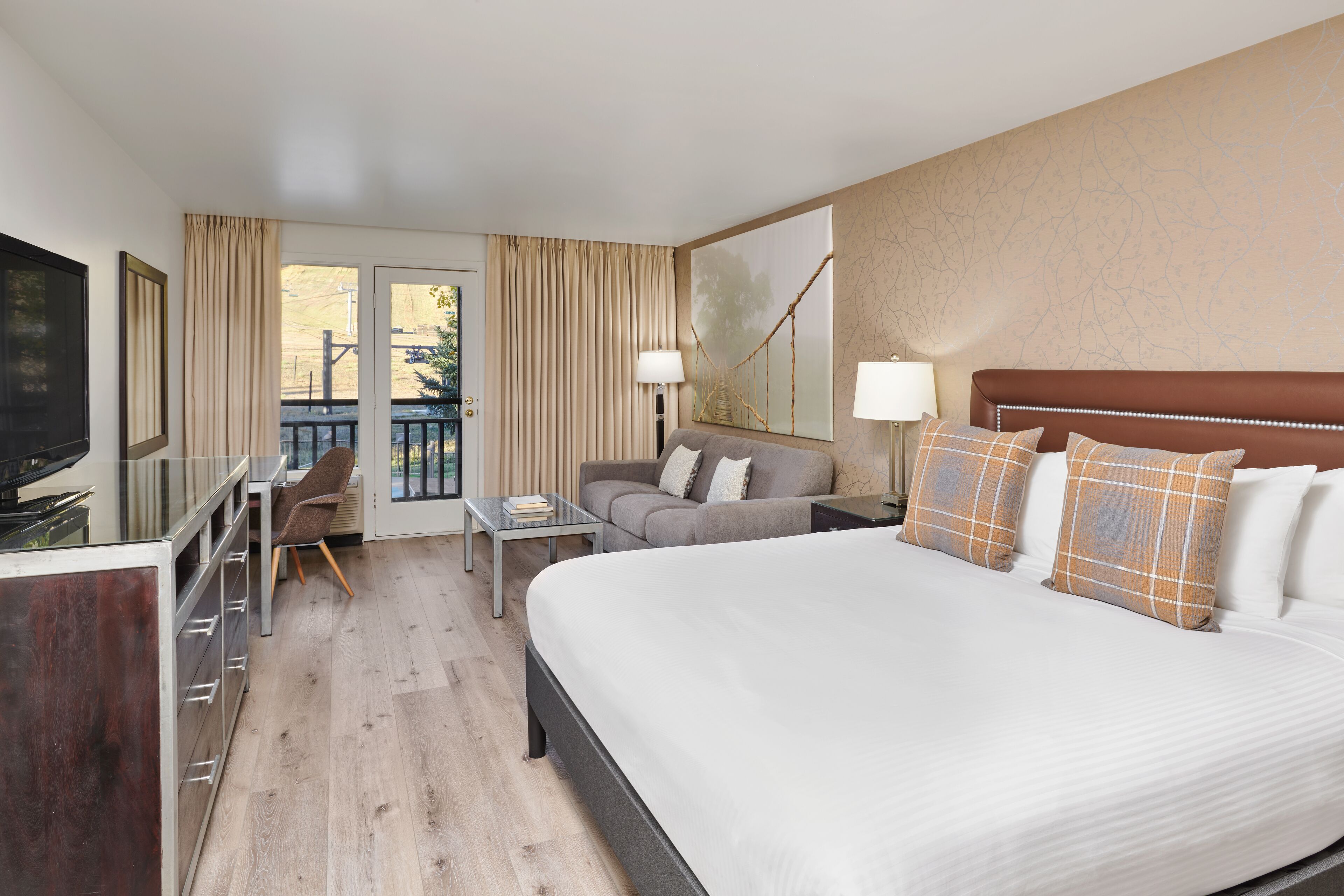 A hotel room with a large bed, a desk, a chair, and a television.
