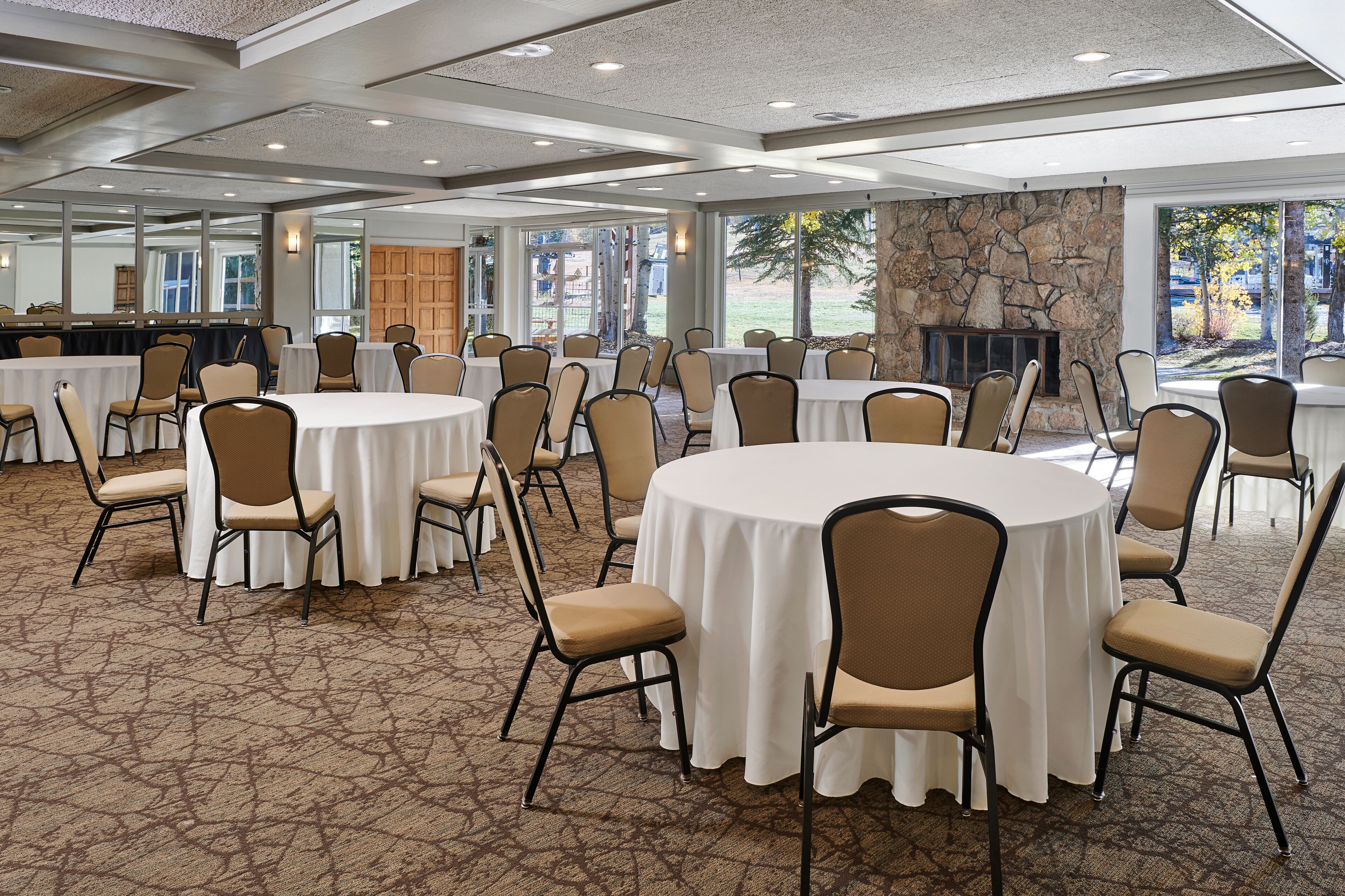 A conference room with round tables, chairs, and a stone fireplace.