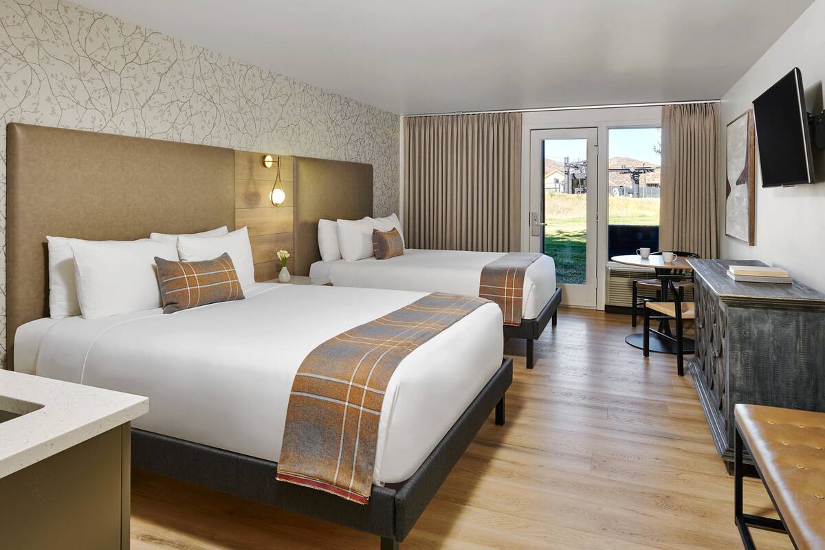 A hotel room with two beds, a desk, a chair, and a television.