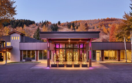 A modern building with a covered entrance, large windows, and a view of a hilly landscape.