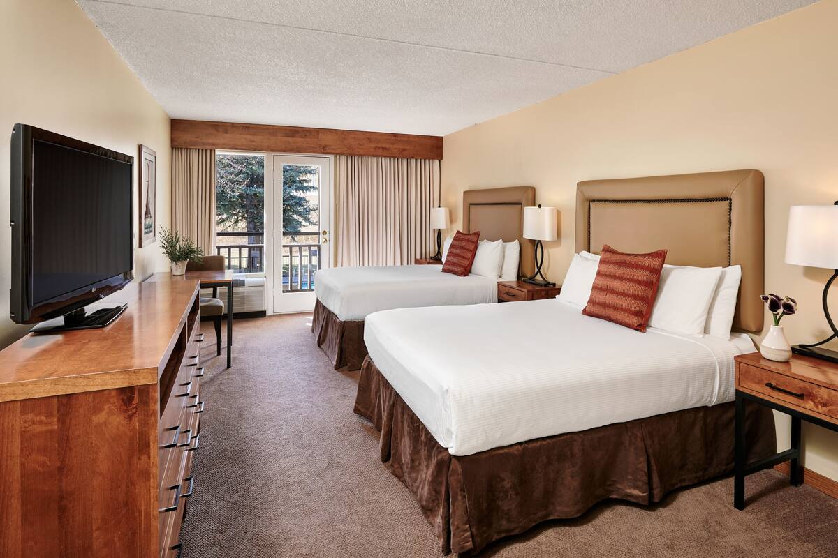 A hotel room with two beds, a TV, a desk, and a balcony.