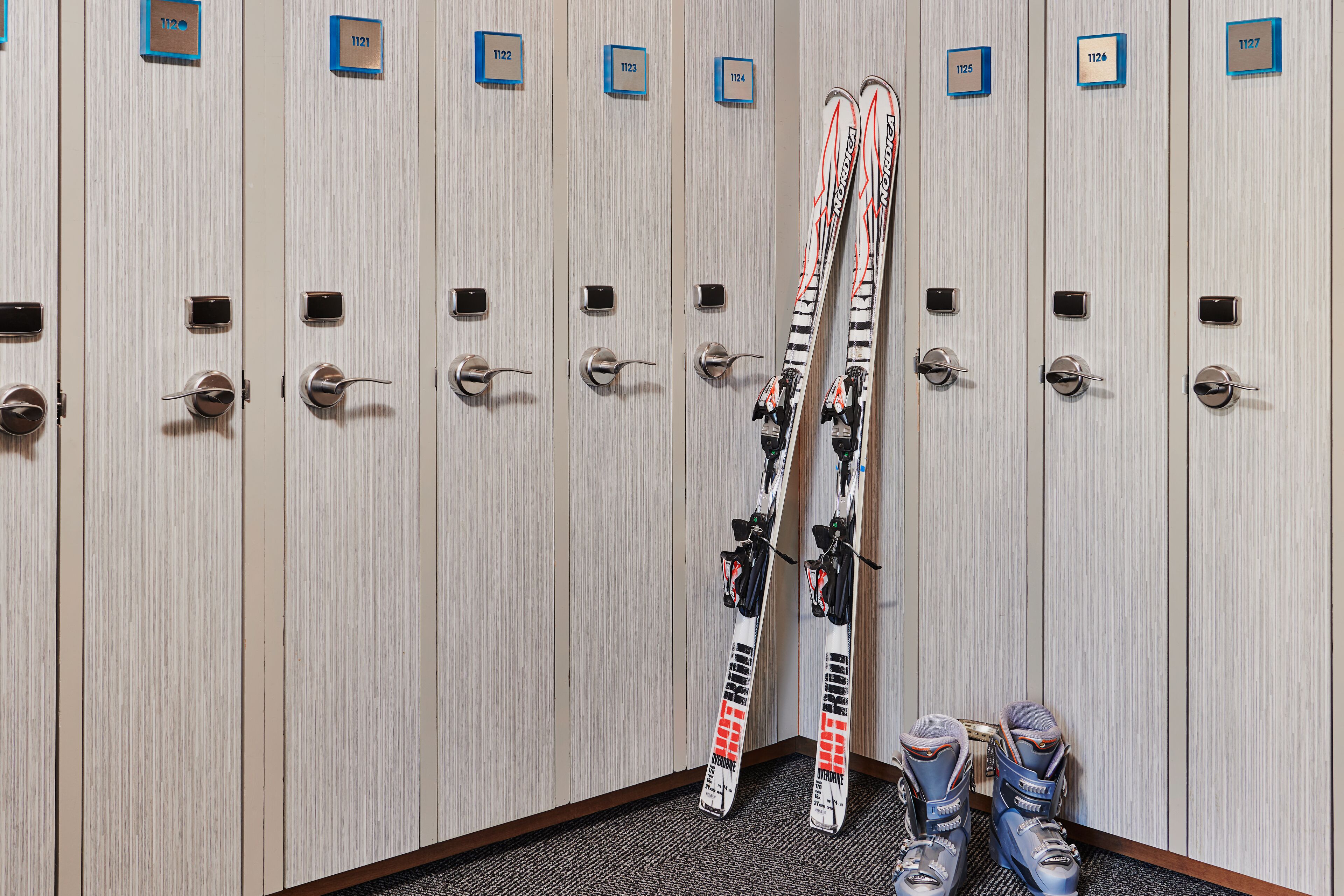 A row of lockers with numbered labels, some with skis and boots placed inside.