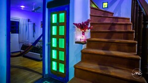 A staircase with wooden steps leading to a landing, a door with green lighting, and a vase with red flowers on a shelf.