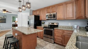 A modern kitchen with granite countertops, stainless steel appliances, wooden cabinets, and a central island with stools. - 3BR w/ Private Pool and Hot Tub in Garden City Beach (Garden City Beach)