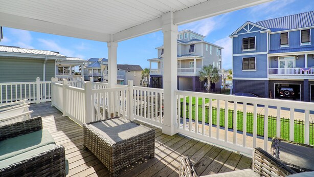 A covered deck with wicker furniture and a white railing, overlooking a residential area with houses and a green lawn. - 3BR w/ Private Pool and Hot Tub in Garden City Beach (Garden City Beach)
