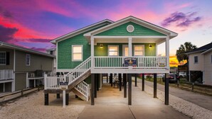 A green house with a white porch and a staircase leading to the entrance. - 3BR w/ Private Pool and Hot Tub in Garden City Beach (Garden City Beach)