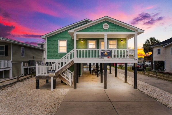 A green house with a white porch and a staircase leading to the entrance. - 3BR w/ Private Pool and Hot Tub in Garden City Beach (Garden City Beach)