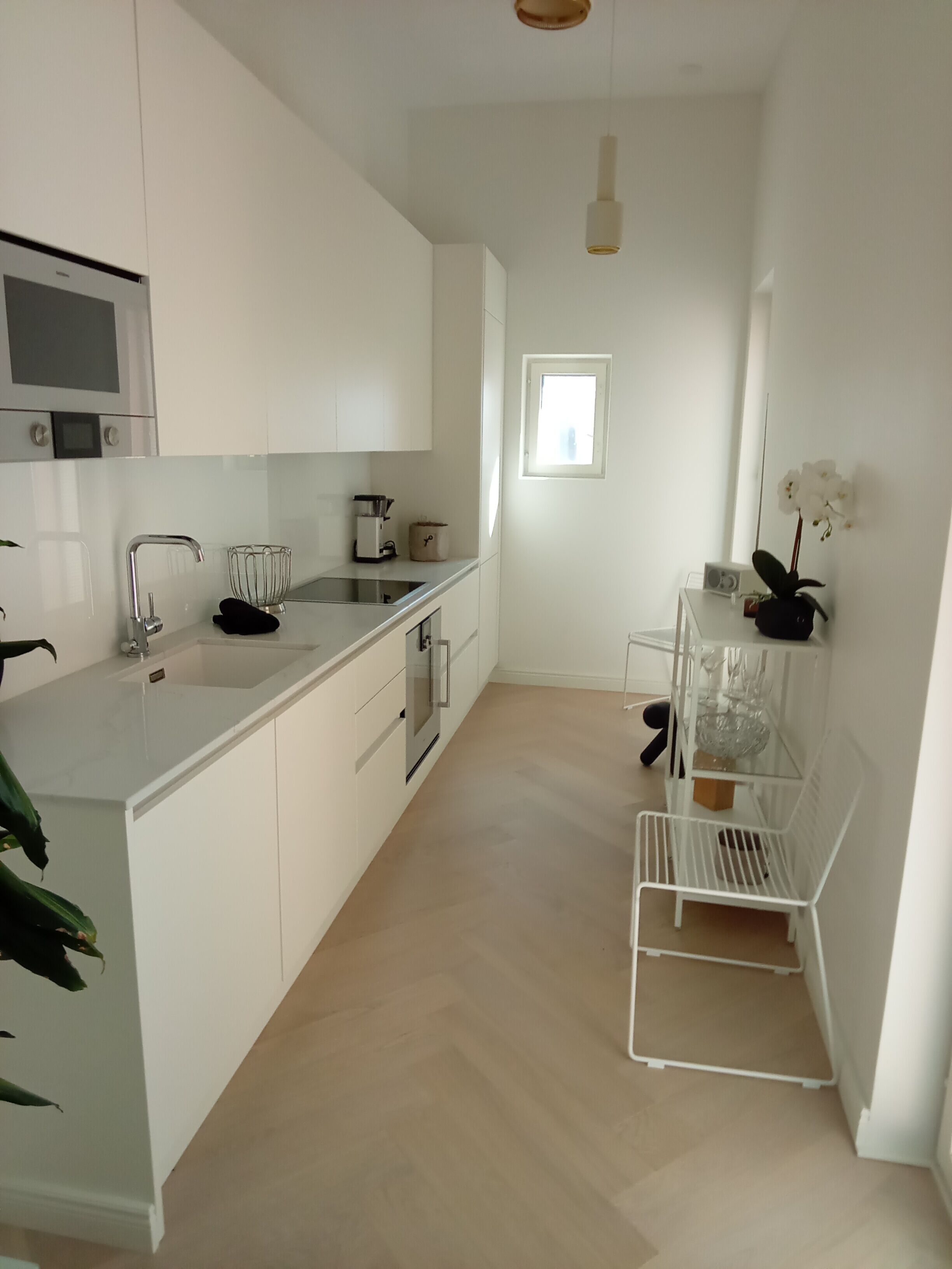 A modern kitchen with white cabinetry, a built-in oven, and a stainless steel sink.