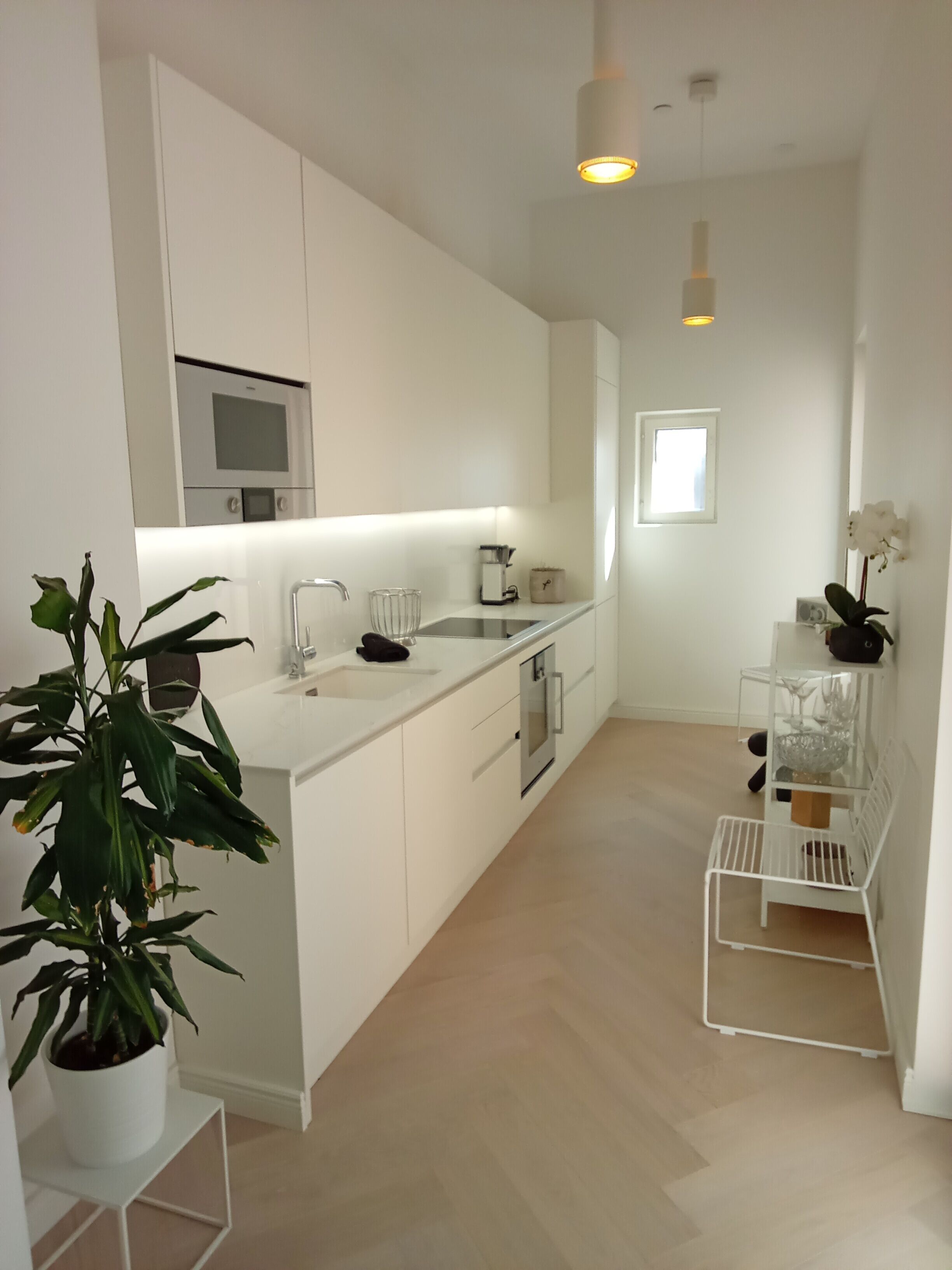 A modern kitchen with white cabinetry, a built-in oven, and a sink. There is a small island with a plant and a glass bowl.