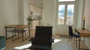 Una sala de estar moderna con sofá, una mesa de comedor con sillas, una zona de cocina y un ventanal con vistas a edificios.