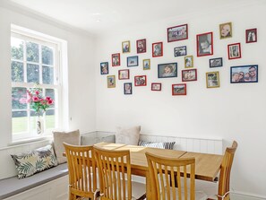 A dining area with a wooden table and chairs, a bench with cushions, and a wall adorned with framed photographs. - The White House - Bordon  - sleeps 10 guests  in 5 bedrooms (Bordon)