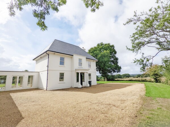 A two-story white house with a gravel driveway and a large tree in the background. - The White House - Bordon  - sleeps 10 guests  in 5 bedrooms (Bordon)