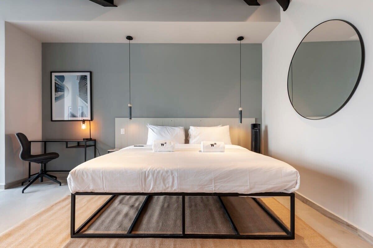 Ein modernes Schlafzimmer mit Bett, Nachttischen, einem Sessel, einem Schreibtisch und einem großen Spiegel.