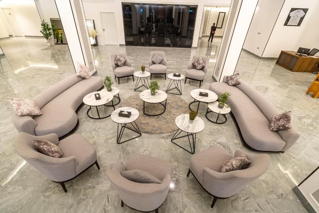 A modern lobby with a circular seating arrangement, marble flooring, and a reception desk in the background.