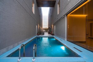 Una piscina interior con vistas despejadas al techo y a las paredes, rodeada por un suelo de baldosas y un techo de madera.