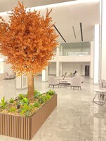 A modern indoor space with a large tree planter, seating area, and a glass railing overlooking the interior.