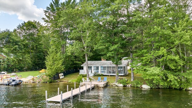 Un chalet au bord du lac, doté d’une jetée qui s’avance dans l’eau, et entouré d’une forêt dense.