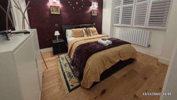 Une chambre à coucher avec un lit, des tables de chevet, une horloge et une fenêtre avec des volets.