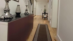 Un couloir doté d’un plancher en bois, d’un tapis à motifs, d’un comptoir d’accueil agrémenté d’objets décoratifs et d’un escalier avec des rampes blanches.