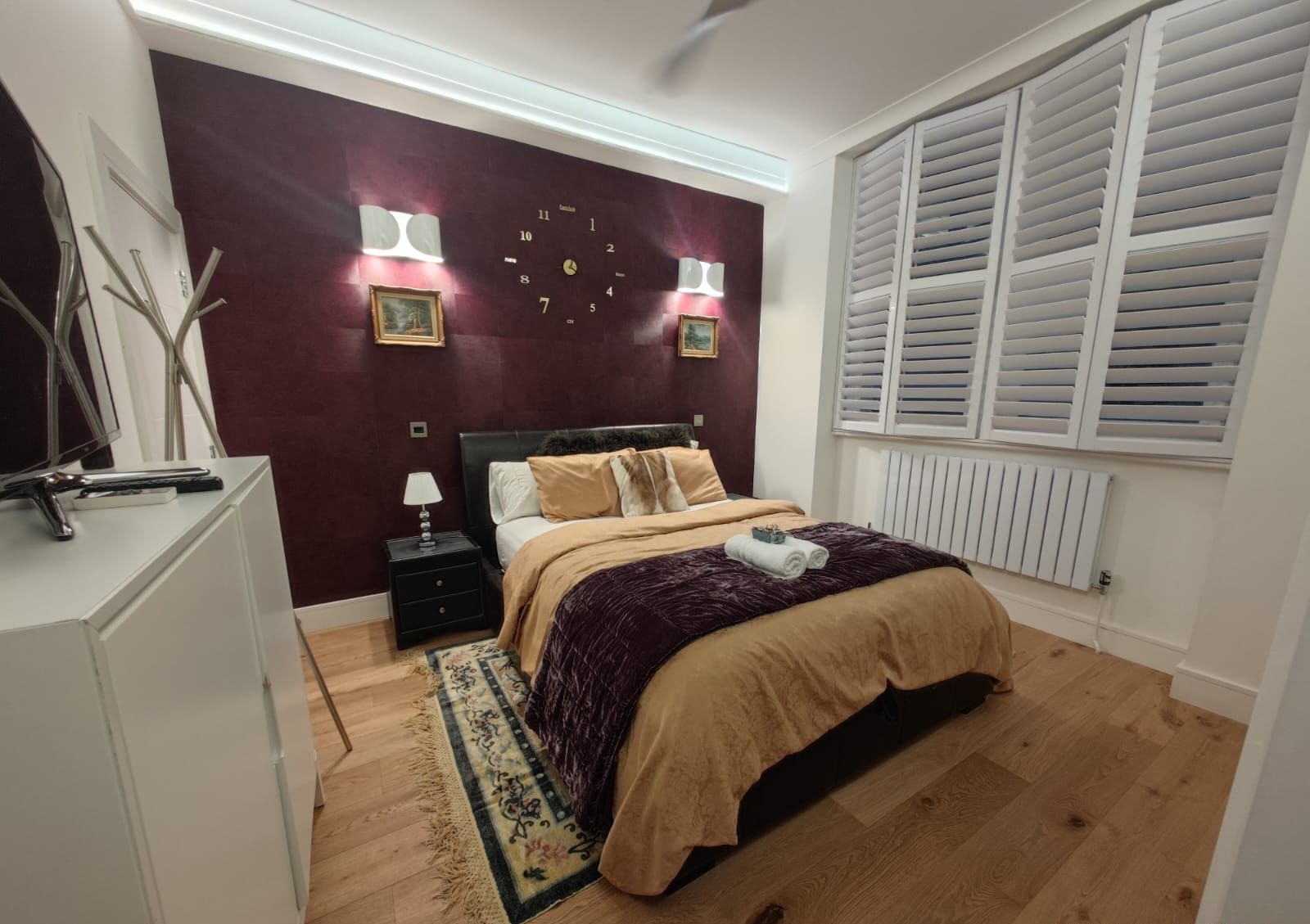 Een slaapkamer met een bed, nachtkastjes, een klok en een raam met luiken.