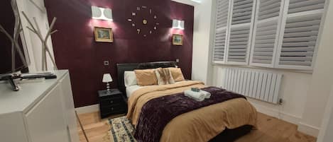 A bedroom with a bed, bedside tables, a clock, and a window with shutters.