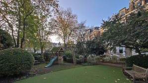 Une aire de jeux avec un toboggan et des structures d’escalade, entourée d’arbres et d’une zone herbeuse.