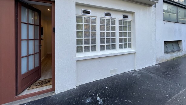 Un edificio con fachada blanca, una puerta de madera con paneles de vidrio y una ventana de múltiples partes.