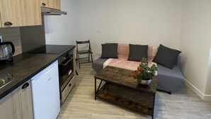 Una cocina compacta con electrodomésticos modernos, un comedor con una mesa de centro y un rincón de estar con sofá y cojines.