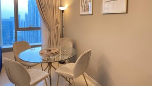 A modern dining area with a glass table, four chairs, a floor lamp, and two framed artworks on the wall. - Lux BnB I 29 Burj BLVD I Downtown Views (Dubai)