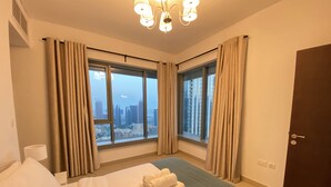 A hotel room with a bed, a view of the cityscape through large windows, a door, and a nightstand with a lamp. - Lux BnB I 29 Burj BLVD I Downtown Views (Dubai)