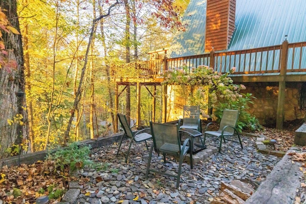 A wooden deck with chairs, surrounded by a forest and a metal roof structure.