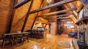 Interior acogedor y rústico de una cabaña, con comedor de madera, cocina y chimenea.