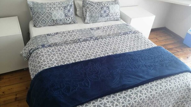 A bed with patterned bedding and pillows, a bedside table, and a wooden floor. - monument pavilion (Gqeberha (Port Elizabeth))