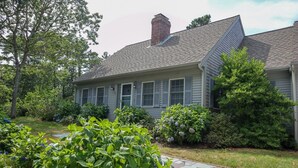 A house with a sloped roof, a brick chimney, and a stone pathway leading to the front door. - Sprawling Home With Great Outdoor Space (2288) (Harwich Port)