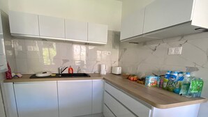 Una cucina moderna con mobili bianchi, una parete di fondo in marmo e un piano di lavoro in legno.