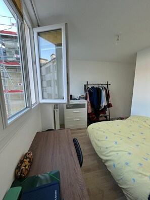 A bedroom with a bed, a desk with a chair, a wardrobe, and a window with blinds.