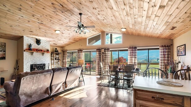 A spacious living area with a wooden ceiling, a fireplace, and a large window overlooking a scenic view. - EpicViews!~EasyRoads!~HotTub~FirePlace~Firepit (Sevierville)