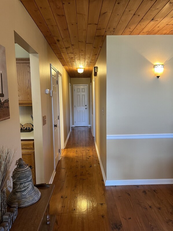 A wooden-paneled hallway with a white door at the end, a light fixture on the wall, and a wooden bench with decorative items. - EpicViews!~EasyRoads!~HotTub~FirePlace~Firepit (Sevierville)