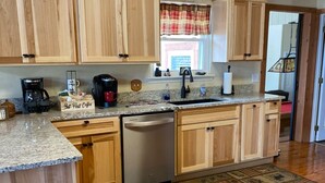 A kitchen with wooden cabinets, a granite countertop, a dishwasher, and a window with plaid curtains. - EpicViews!~EasyRoads!~HotTub~FirePlace~Firepit (Sevierville)