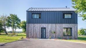 Een modern huis met twee verdiepingen, een donkere gevel, een voordeur en twee ramen op de bovenverdieping.
