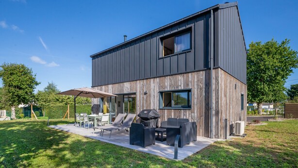 Een moderne, twee verdiepingen tellende woning met een terras en tuinmeubilair.