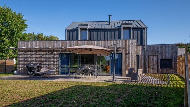 Una casa moderna con un patio amueblado con mobiliario exterior y un paraguas grande.