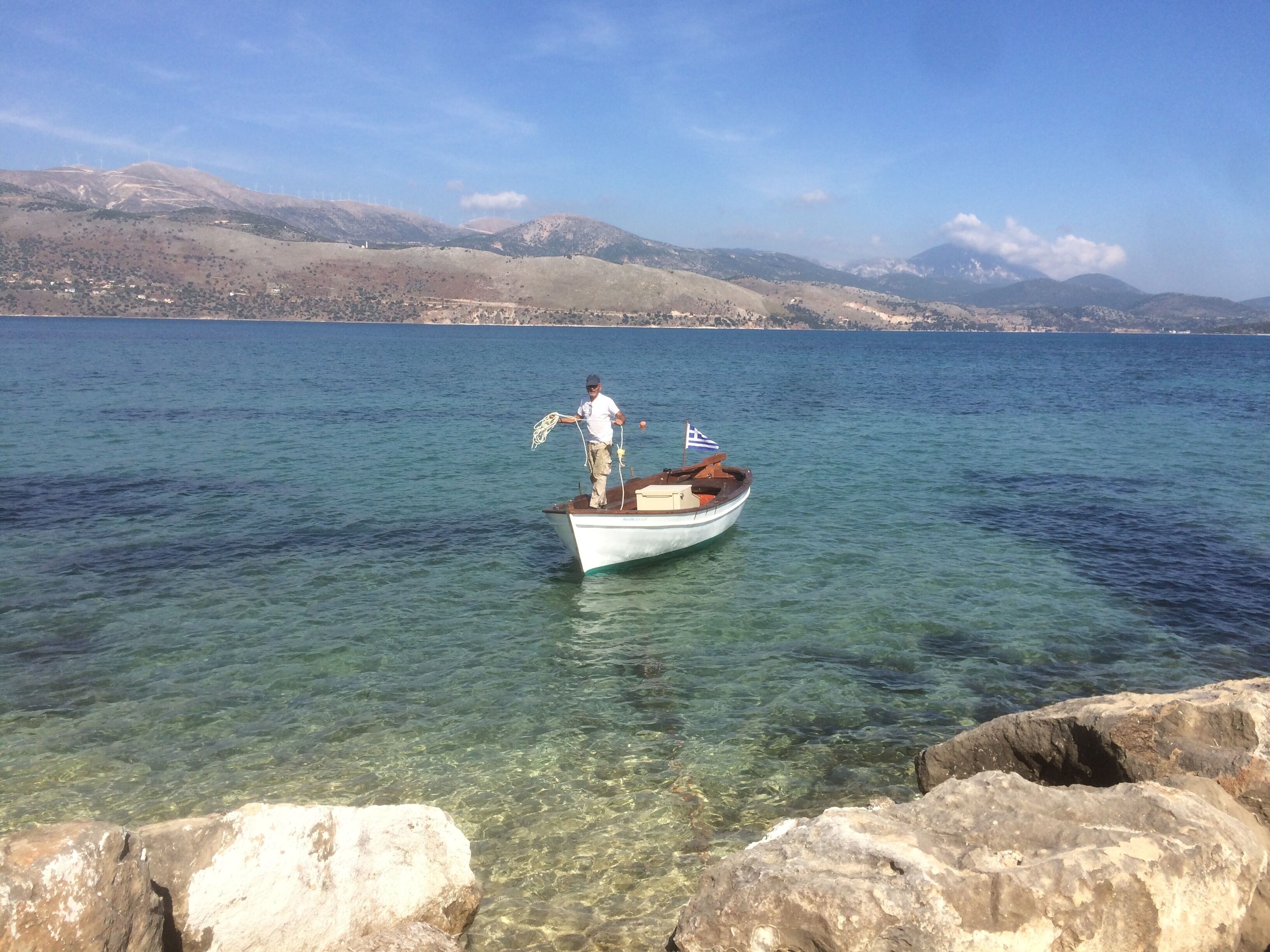 A boat with a flag on a calm body of water, surrounded by rocky shores and distant mountains.