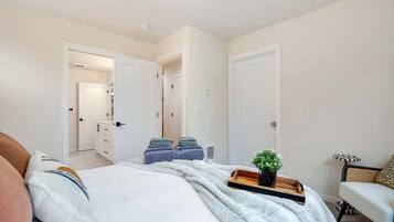 Ein Schlafzimmer mit einem Bett, Nachttischen, einem Sessel und einer Tür zu einem anderen Raum.